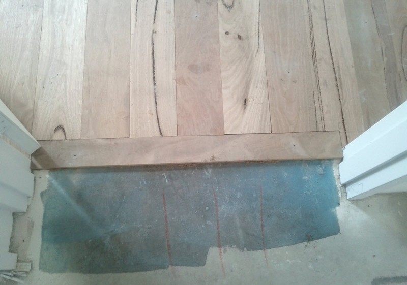 Marri floorboards - raw and unsealed, showing the finish along a doorway, with transition to future tiles.